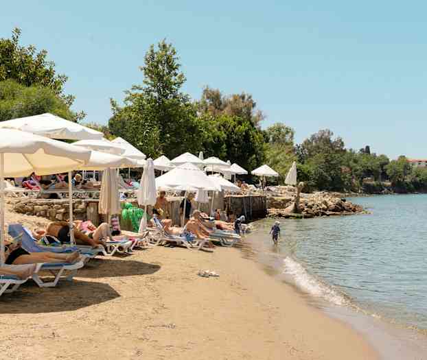 Uimaranta, jossa on aurinkotuoleja ja aurinkovarjoja kirkkaan veden äärellä. (Tekoälyn luoma teksti)