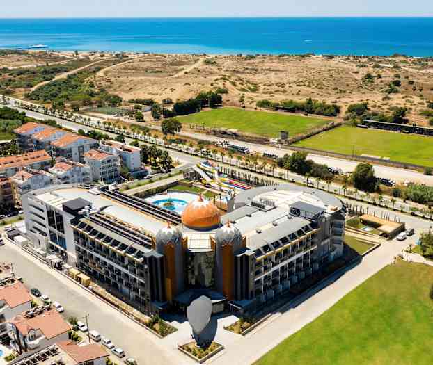 Hotelli, jossa on ainutlaatuinen arkkitehtuuri, lähellä merta, ympäröitynä kasvillisuudella ja vihreillä alueilla. (Tekoälyn luoma teksti)