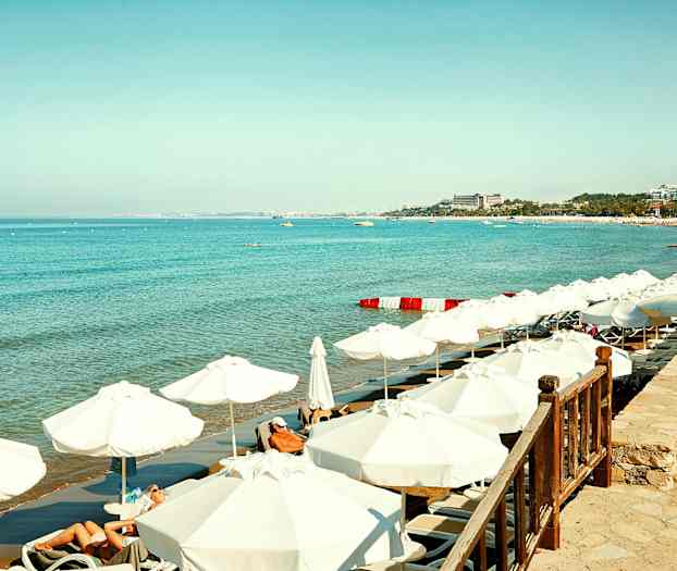 Valkoinen hiekkaranta aurinkotuoleilla ja varjoilla kirkkaan sinisen meren äärellä. (Tekoälyn luoma teksti)