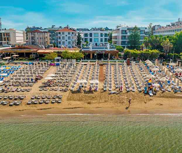 Ranta aurinkotuoleilla ja varjoilla, ympärillä hotelleja ja rakennuksia. (Tekoälyn luoma teksti)