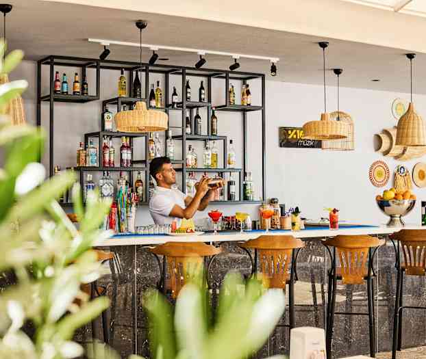 Baari, jossa hyllyt täynnä pulloja ja kolme puista tuolia edessä. (Tekoälyn luoma teksti)