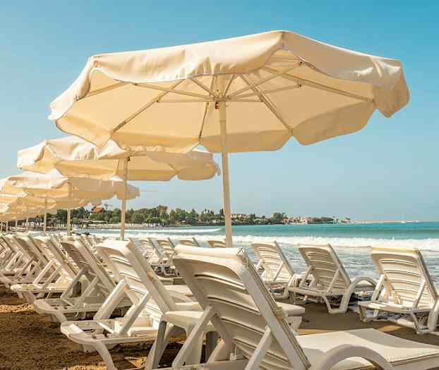 Rivi aurinkotuoleja ja aurinkovarjoja hiekkarannalla, näkymä merelle. (Tekoälyn luoma teksti)