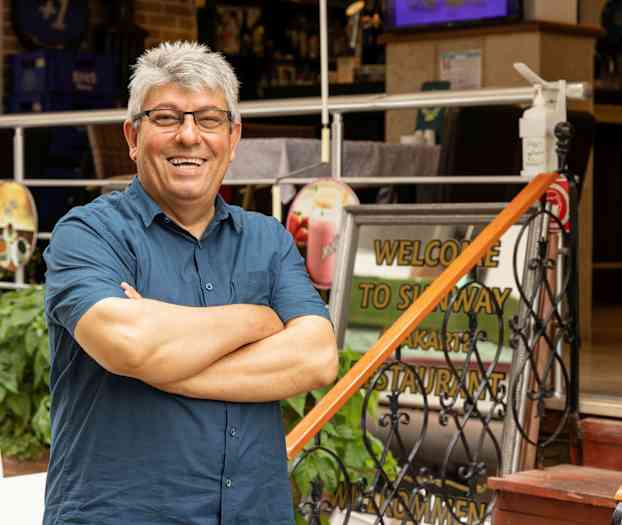 Henkilö seisoo kädet ristissä ravintolan sisäänkäynnin edessä, jossa näkyy tervetulokyltti. (Tekoälyn luoma teksti)