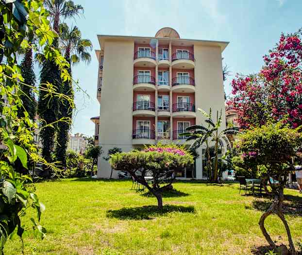 Kerrostalo, jossa on parvekkeita, ympäröity vihreydellä ja kukkivilla puilla etualalla. (Tekoälyn luoma teksti)