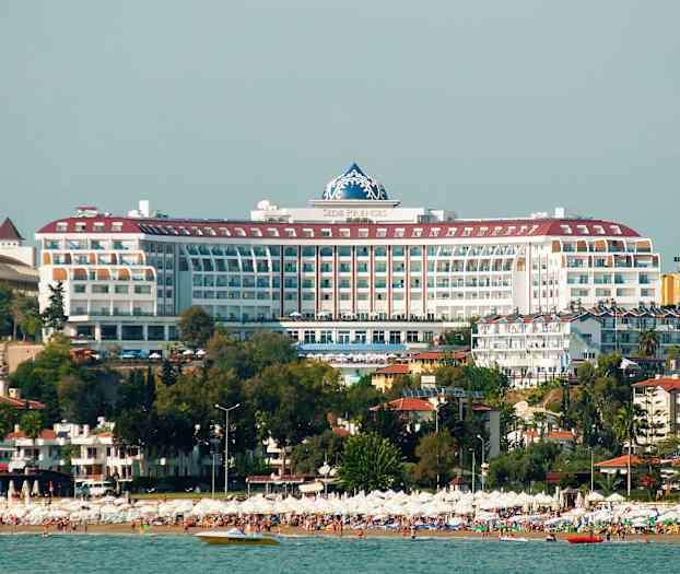 Suuri ranta aurinkovarjoineen ja hotellirakennus taustalla. (Tekoälyn luoma teksti)