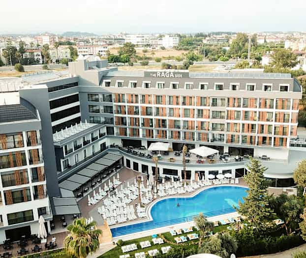 Ilmakuva hotellirakennuksesta, jossa on uima-allasalue ja aurinkotuoleja edessä. (Tekoälyn luoma teksti)