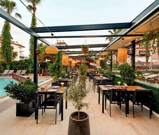 Ulkoterassi uima-altaan vieressä, jossa on pöytiä ja tuoleja sekä kasveja ja valaistus. (Tekoälyn luoma teksti)