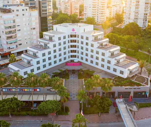 Nykyaikainen hotelli vihreyden ja muiden rakennusten ympäröimänä, nähtynä ylhäältä. (Tekoälyn luoma teksti)