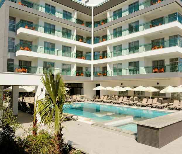 Hotellirakennus moderneilla parvekkeilla ja uima-allas, jota ympäröivät aurinkotuolit ja varjot. (Tekoälyn luoma teksti)