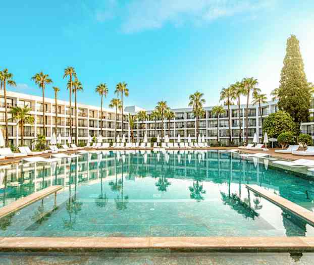 Hotellin uima-allas, jonka ympärillä aurinkotuoleja ja päivänvarjoja, palmupuita ja moderneja rakennuksia. (Tekoälyn luoma teksti)