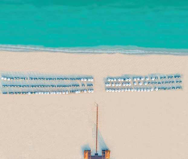 Ilmakuva rannasta, jossa aurinkotuoleja ja aurinkovarjoja meren äärellä. (Tekoälyn luoma teksti)