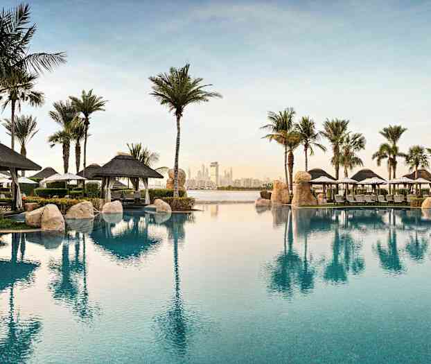 Näkymä uima-altaalta lomakeskus-rakennusten edessä, palmuja ja aurinkovarjoja. (Tekoälyn luoma teksti)