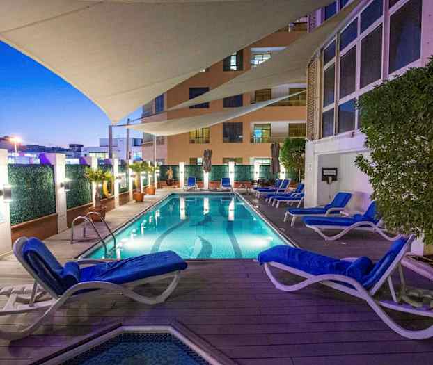 Valaistu uima-allas, jota ympäröivät aurinkotuolit ja kasvit, suojakankaan alla illalla. (Tekoälyn luoma teksti)