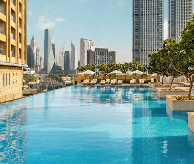 Infinity-allas, jota ympäröivät aurinkotuolit ja aurinkovarjot, korkeat rakennukset taustalla. (Tekoälyn luoma teksti)