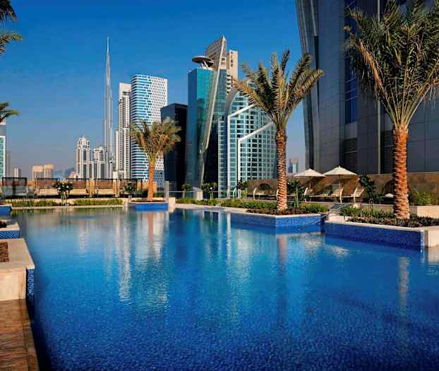 Uima-allas, jota ympäröivät palmut, taustalla nykyaikaisia rakennuksia. (Tekoälyn luoma teksti)