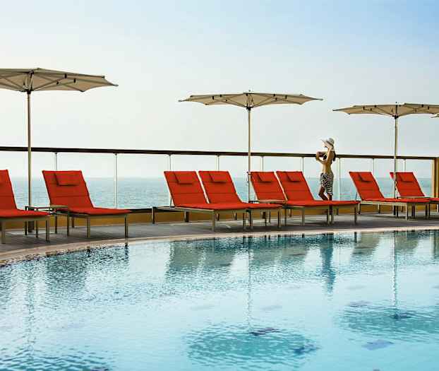 Ulkouima-allas, jonka reunalla on punaisia aurinkotuoleja ja valkoisia varjoja, taustalla merinäkymä. (Tekoälyn luoma teksti)