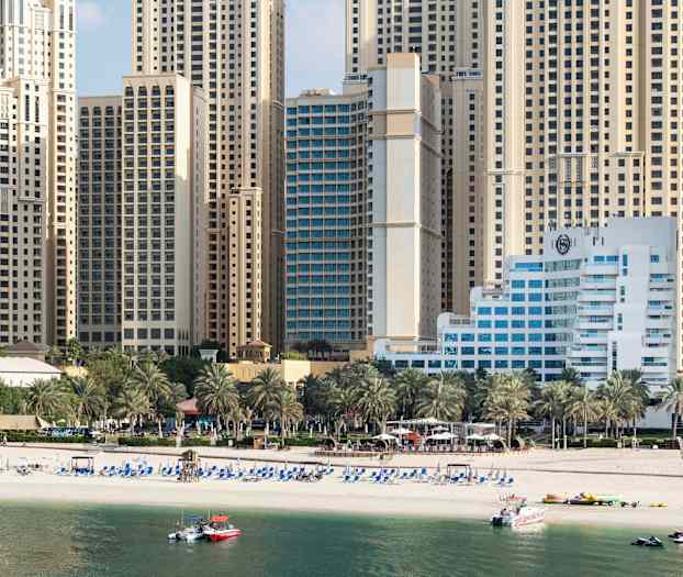 Korkeat rakennukset taustalla, edessä ranta ja palmuja. (Tekoälyn luoma teksti)