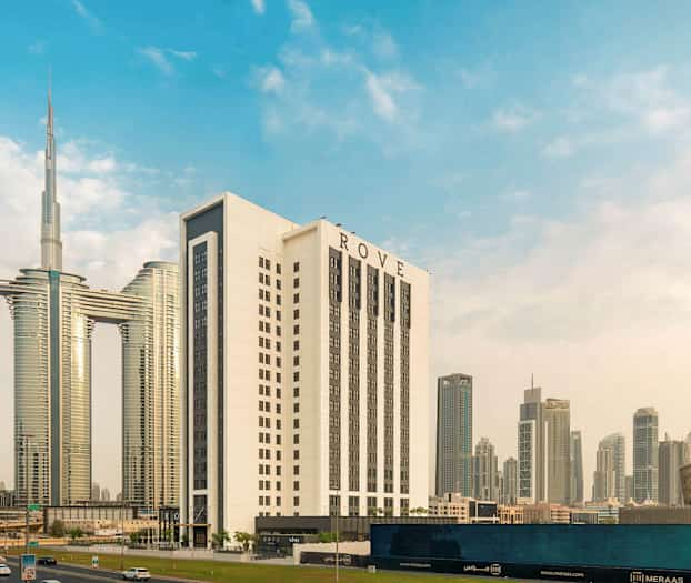 Moderni kaupunkimaisema, joka sisältää useita korkeita rakennuksia, mukaan lukien suurempi valkoinen hotelli nimeltä ROVE, ympäröitynä muilla pilvenpiirtäjillä ja arkkitehtonisilla rakenteilla. (Tekoälyn luoma teksti)