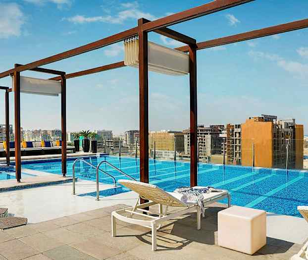 Ulkouima-allas, josta on näkymä kaupunkiin. Altaan ympärillä on aurinkotuoleja, pöytiä ja koristeita. (Tekoälyn luoma teksti)