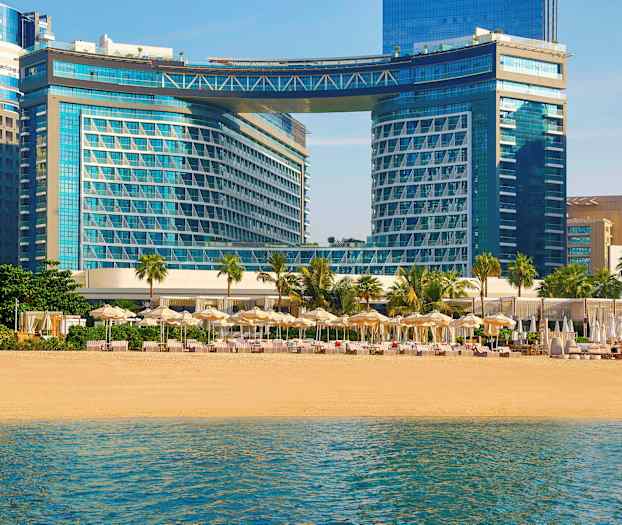 Modernit rakennukset rannalla, jossa aurinkovarjoja ja aurinkotuoleja. (Tekoälyn luoma teksti)