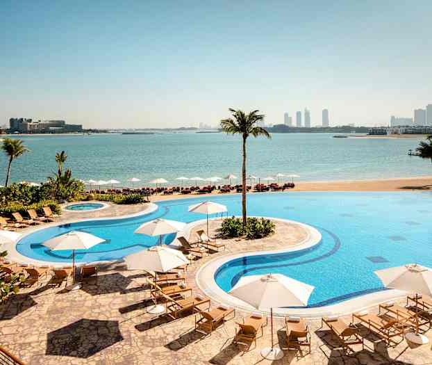 Hotellin uima-allas aurinkotuoleineen ja aurinkovarjoineen, rannalla merelle ja taustalla olevaan kaupunkiin avautuvalla näkymällä. (Tekoälyn luoma teksti)