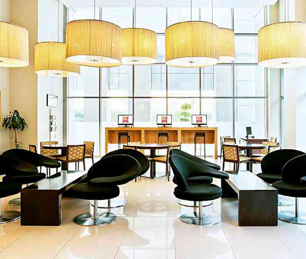 Moderni hotellin aula, jossa on mustia tuoleja, pöytiä ja tietokonepisteitä. (Tekoälyn luoma teksti)