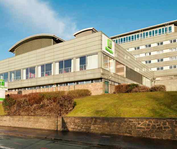 Holiday Inn -hotelli modernissa rakennuksessa, jota ympäröivät nurmikko ja pensaat. (Tekoälyn luoma teksti)