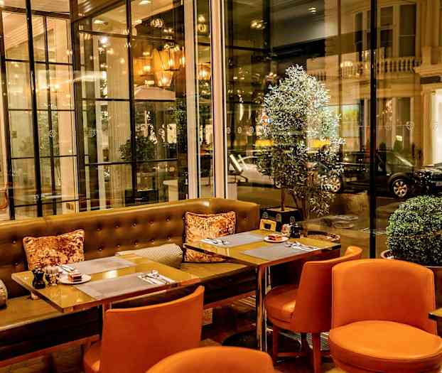 Ravintola, jossa on oransseja tuoleja ja lasiseinät, jotka avautuvat kadulle. (Tekoälyn luoma teksti)