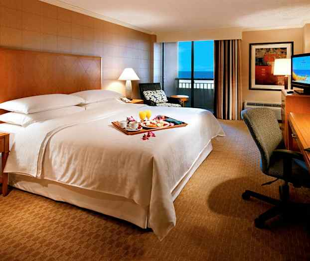 Hotellihuoneen makuuhuone, jossa on suuri sänky, yöpöytä, kirjoituspöytä ja ikkuna, josta on näkymä. (Tekoälyn luoma teksti)