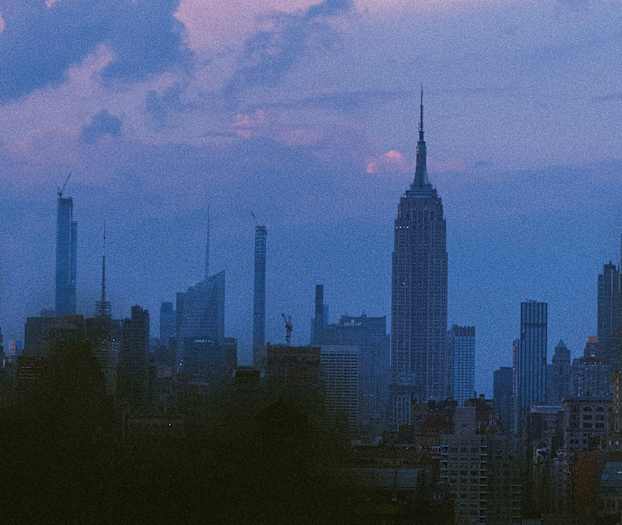 Näkymä kaupungin horisonttiin hämärässä, useita pilvenpiirtäjiä värikkään taivaan edessä. (Tekoälyn luoma teksti)