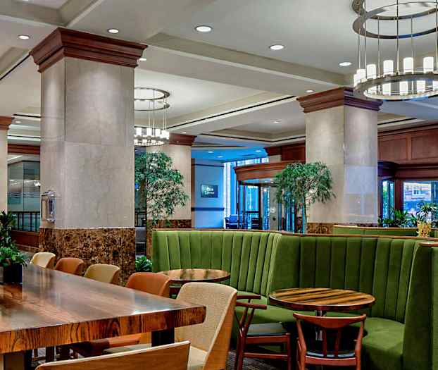 Modernisti sisustettu tila vihreillä looseilla ja puupöydillä, ympärillä kasveja ja valaistusta. (Tekoälyn luoma teksti)