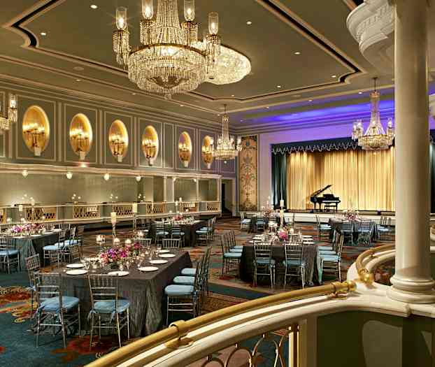 Tyylikäs juhlasali, jossa on kattokruunut, katettuja pöytiä ja lava, jolla on flyygeli. (Tekoälyn luoma teksti)