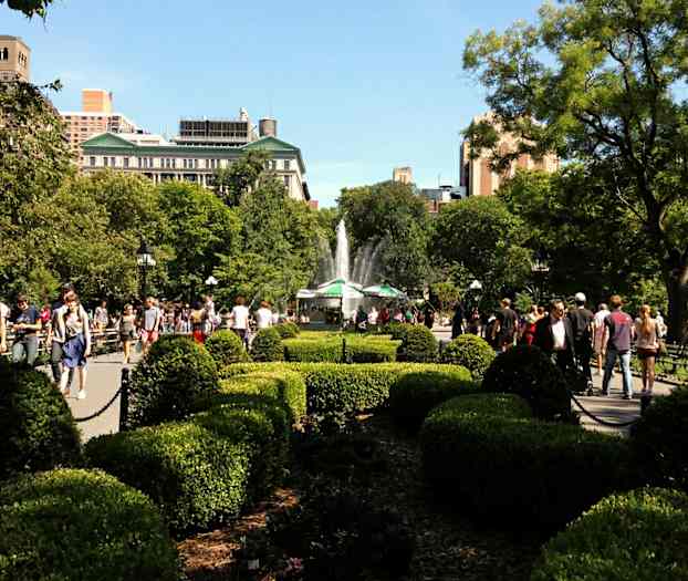 Puisto, jossa on pensaita, puita ja suihkulähde taustalla, jossa ihmiset kävelevät ja oleskelevat. (Tekoälyn luoma teksti)