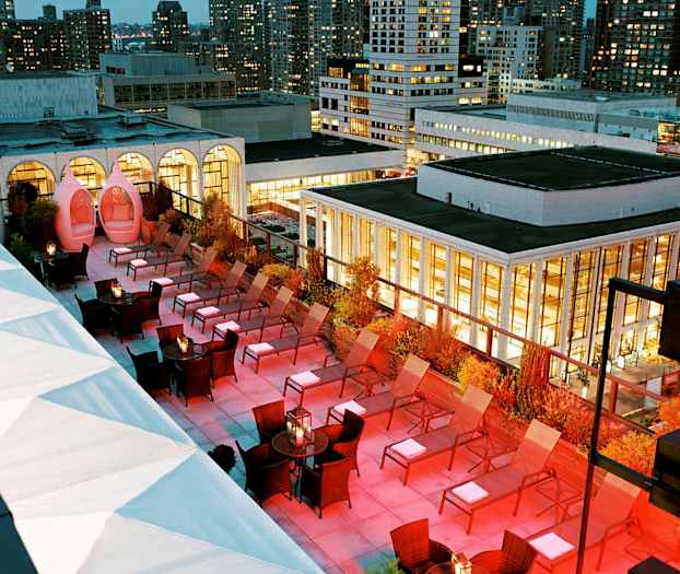 Kattoterassi, jolla on aurinkotuoleja ja illan valaistus, ympäröitynä rakennuksilla. (Tekoälyn luoma teksti)