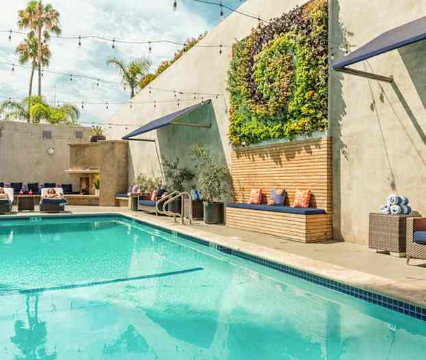 Ulkouima-allas, jossa on aurinkotuoleja, vihreitä kasveja seinällä ja istumapaikkoja tyynyillä. (Tekoälyn luoma teksti)