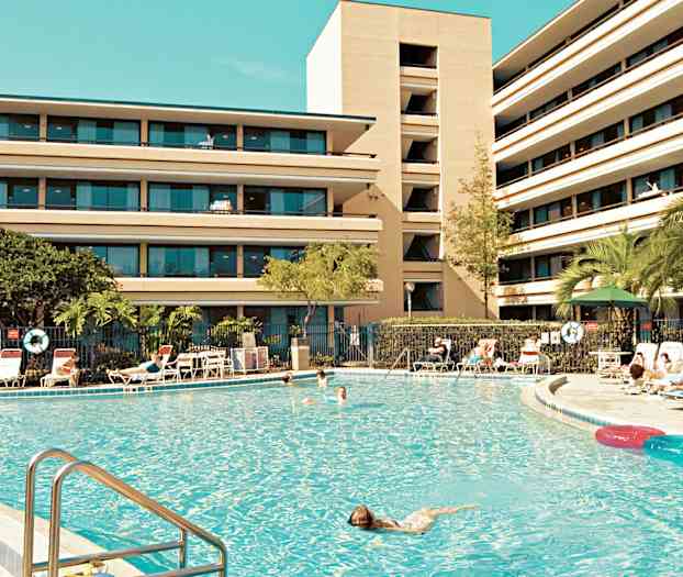 Suuri uima-allas, jota ympäröivät aurinkotuolit, ja taustalla monikerroksinen rakennus. (Tekoälyn luoma teksti)