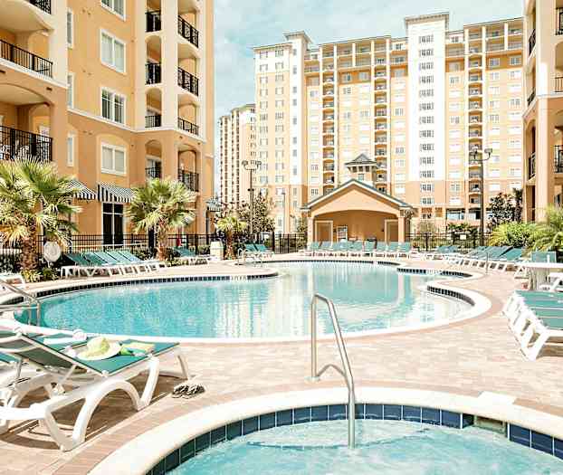 Kuva ulkouima-altaasta, jota ympäröivät aurinkotuolit ja monikerroksiset rakennukset. (Tekoälyn luoma teksti)