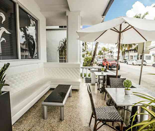 Ulkoterassi, jossa on valkoisia kalusteita ja aurinkovarjoja kaupunkimiljöössä. (Tekoälyn luoma teksti)