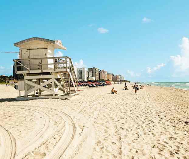 Ranta, jossa on hengenpelastajatorni etualalla ja rakennuksia taustalla. (Tekoälyn luoma teksti)