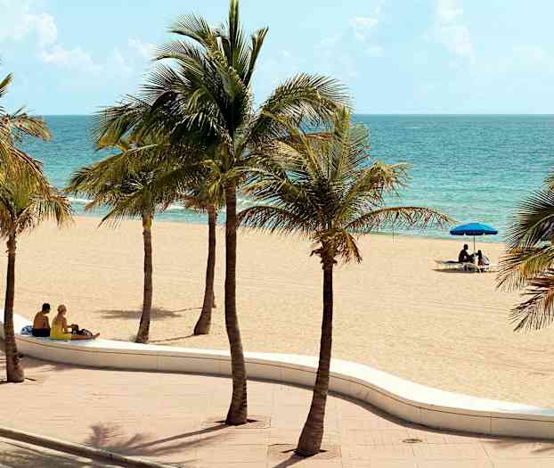 Hiekkaranta, jossa palmuja, ja pari istuu penkillä lähellä rantaa. (Tekoälyn luoma teksti)