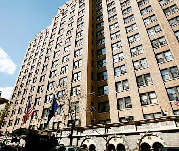 Korkea rakennus, jossa on ruskea julkisivu ja paljon ikkunoita, liput ja sisäänkäynnit alhaalla. (Tekoälyn luoma teksti)