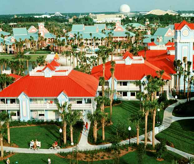 Kuva lomakeskuksesta, jossa on rakennuksia punaisilla katoilla ja vaaleansinisillä julkisivuilla, palmupuita ja kävelyteitä. (Tekoälyn luoma teksti)