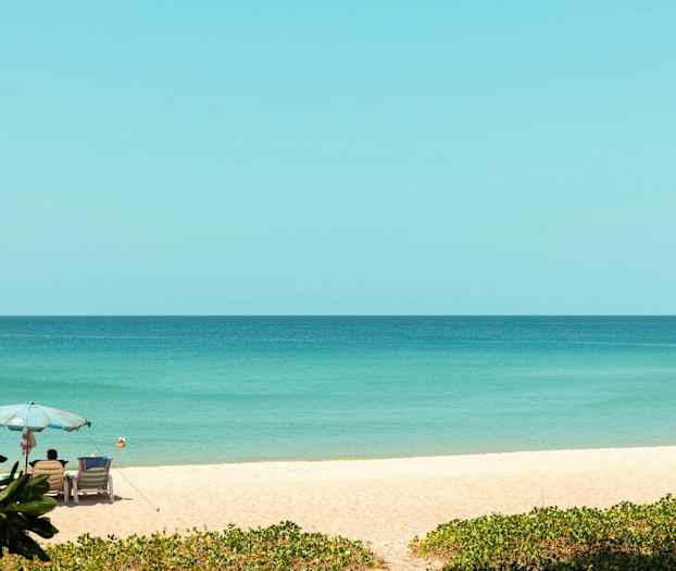 Hiekkaranta, jossa on sateenvarjo ja aurinkotuoleja lähellä merta. (Tekoälyn luoma teksti)