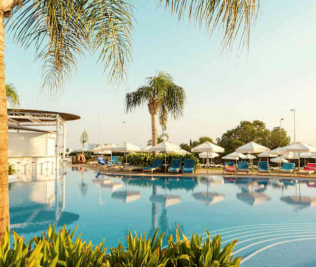 Uima-allas, jonka ympärillä on aurinkotuoleja, joissa on sinisiä ja punaisia tyynyjä, aurinkovarjoja ja palmuja. (Tekoälyn luoma teksti)