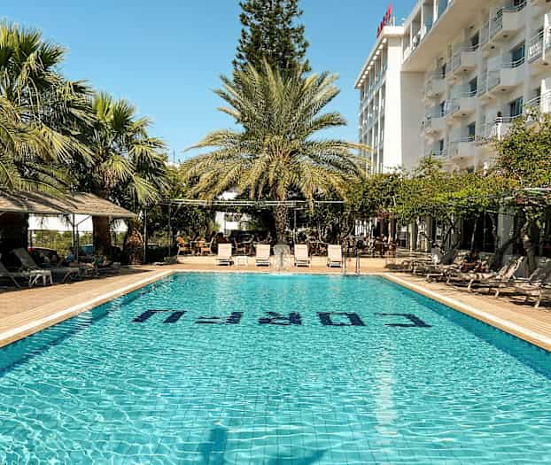 Ulkoallas, jossa aurinkotuoleja ja palmuja hotellirakennuksen vieressä. (Tekoälyn luoma teksti)