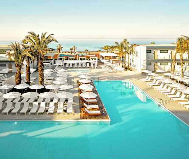 Hotellin uima-allas, jota ympäröivät aurinkotuolit ja aurinkovarjot, taustalla palmuja ja merinäkymä. (Tekoälyn luoma teksti)