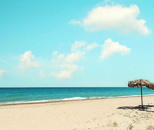 Hiekkaranta, jossa aurinkovarjo, meri taustalla. (Tekoälyn luoma teksti)