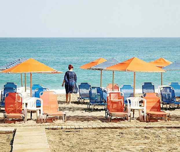 Ranta aurinkotuoleilla ja aurinkovarjoilla, henkilö kävelee kohti merta. (Tekoälyn luoma teksti)