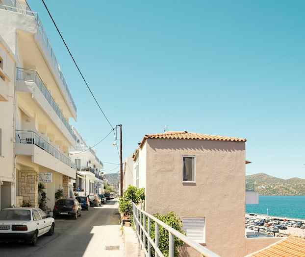 Katu, jolla on pysäköintialue ja monikerroksisia taloja meren rannalla. (Tekoälyn luoma teksti)