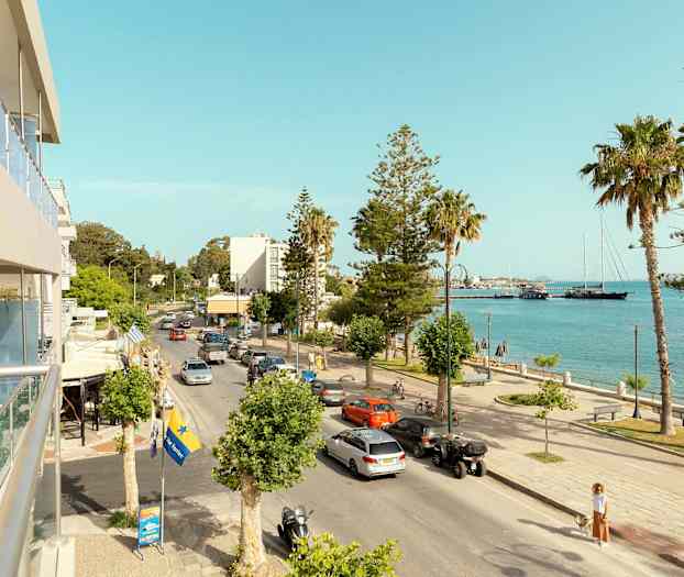 Kaupunkikatu, joka kulkee meren vieressä, autojen, palmujen ja muutamien rakennusten kanssa taustalla. (Tekoälyn luoma teksti)